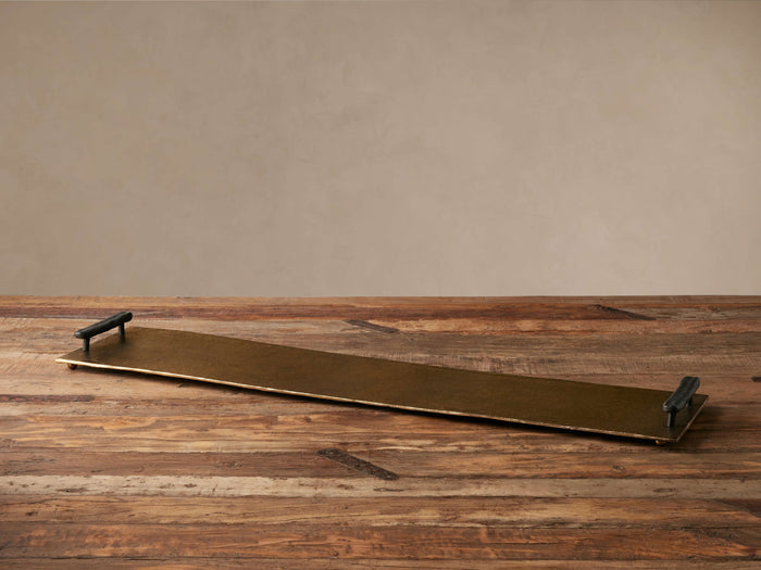 Pasca Rectangular Tray with antique brass finish and dark handles, on a rustic wood table, viewed from above.