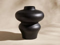 Pelle Vase. Matte ebony-finished aluminum vase with a unique bulbous shape: wide top, narrow middle, flaring base, on light ground.