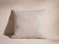 Light pink Phare Pillow with woven off-white floral pattern & corded edge, standing upright against a textured background.