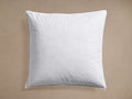 A soft, plump, white square Pillow Insert, viewed from above on a muted beige background, showing its stitched edge.