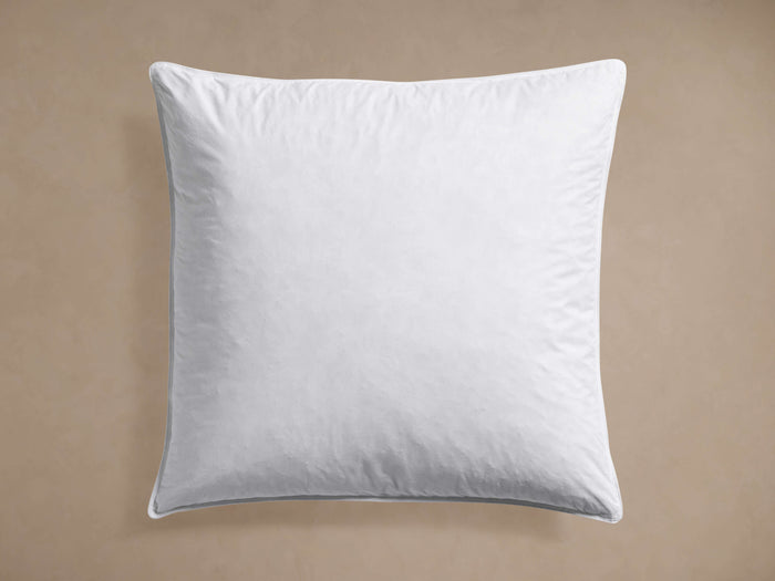 A soft, plump, white square Pillow Insert, viewed from above on a muted beige background, showing its stitched edge.