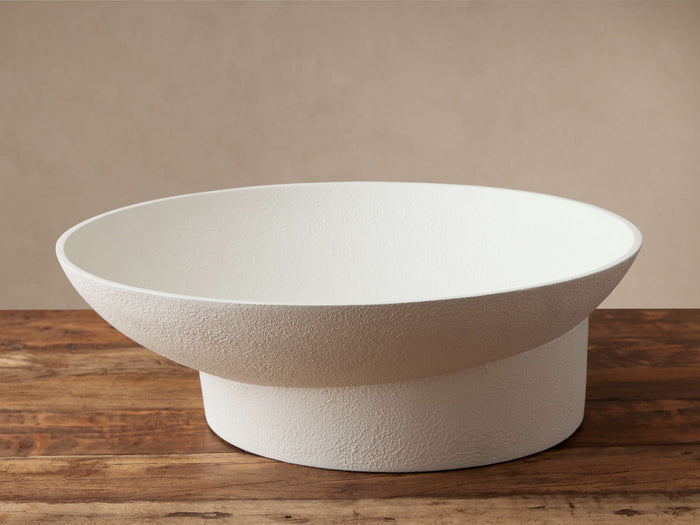 White stucco Planes Footed Bowl, wide and shallow, with a textured surface, sits on a rustic wooden table.
