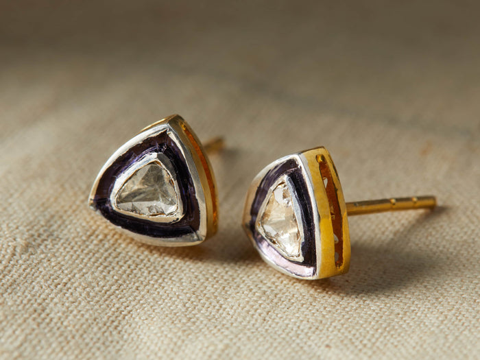Polki Diamond Stud Earrings featuring triangular-shaped diamonds set in gold with dark accents, resting on a textured surface.