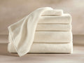 A stack of four thick, cream-colored bath towels with a smooth texture, neatly folded on a neutral background.
