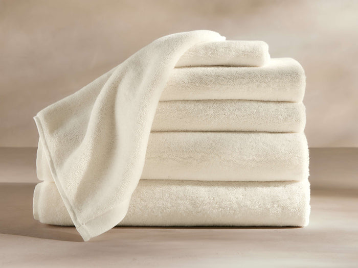 A stack of four thick, cream-colored bath towels with a smooth texture, neatly folded on a neutral background.