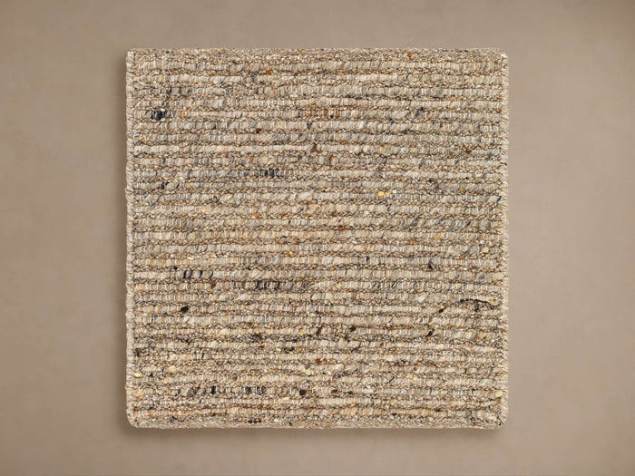 Square Ranna Rug Swatch. Coarse, flat woven natural fibers in beige, tan, brown, and black flecks on a neutral background.