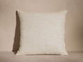 Square off-white Raw Silk Pillow with visible hand-spun texture and subtle tan variations, resting upright against a neutral wall.