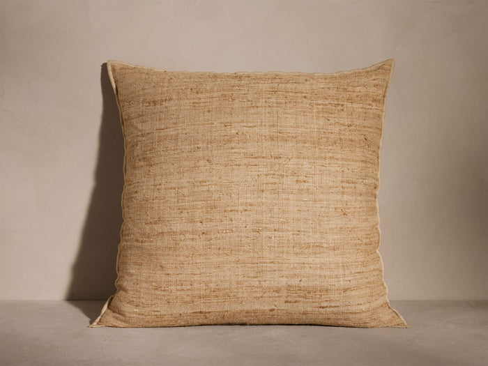 Square natural beige Raw Silk Pillow with visible raw texture and subtle variations, standing upright against a light neutral wall.