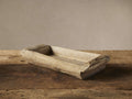 Rectangular reclaimed wood tray with rough, light brown aged patina texture, angled on a rustic wooden table against a pale wall.