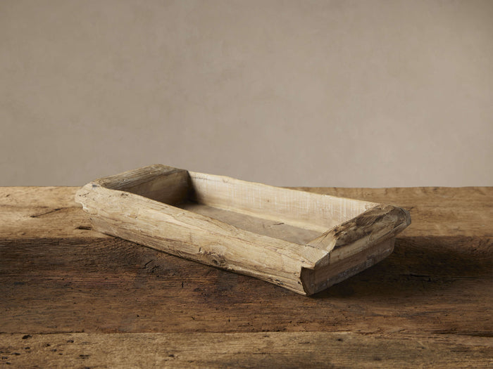 Rectangular reclaimed wood tray with rough, light brown aged patina texture, angled on a rustic wooden table against a pale wall.