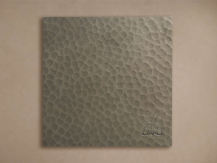 A square, dark grey Recycled Metal Finish Board with a textured hammered surface and an embossed butterfly design in the lower right.