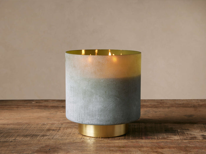 Retreat Olive Fig Candle in frosted glass, fading grey-green to yellow, with an antique brass base & lit wicks.
