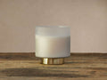 Frosted glass Retreat Tobacco Amber Candle on a wooden surface, with an antique brass base, against a mottled grey background.
