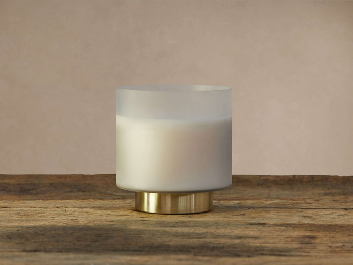 Frosted glass Retreat Tobacco Amber Candle on a wooden surface, with an antique brass base, against a mottled grey background.