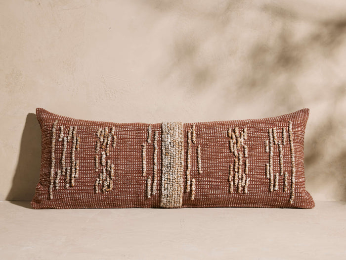 Reyes Outdoor Pillow, rectangular terracotta pillow with textured cream jacquard vertical patterns, lying on a light surface.