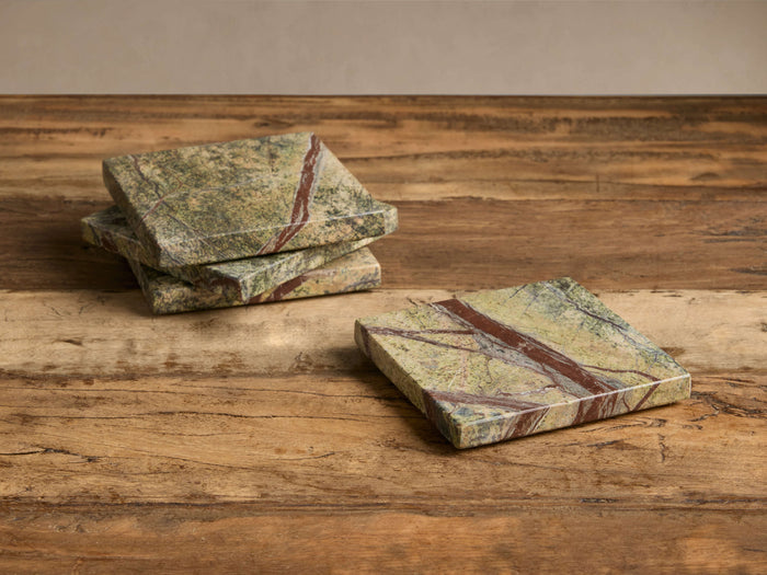 Four Rhodes Coasters, green marble with reddish-brown veins. Three stacked left, one flat right on a rustic wooden surface.