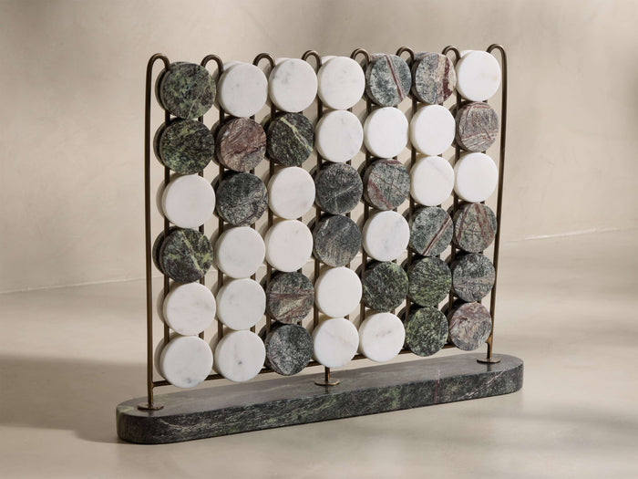 Front view of the Rhodes Four in a Row game, featuring an antique brass rack and dark green marble base, with round white, green, and brown/grey marble game pieces inserted.