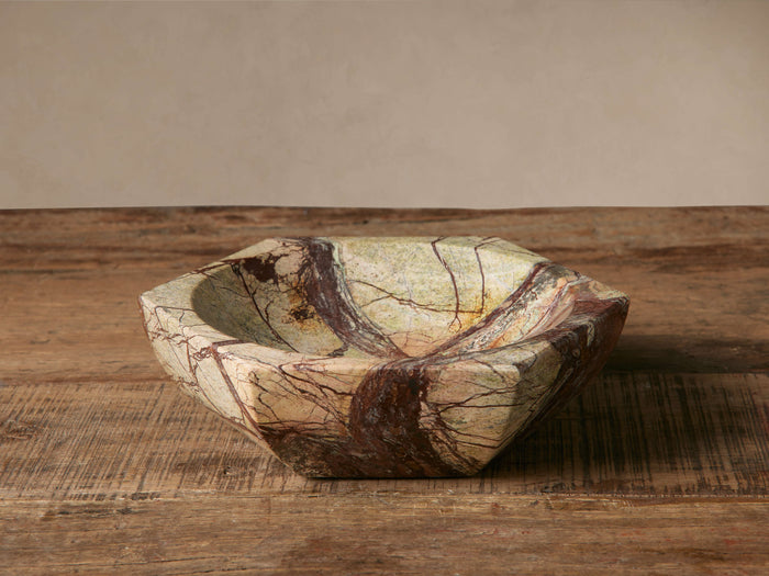Hexagonal Rhodes Marble Bowl, light green/beige with striking dark red/brown veins, sits on a rustic wooden table.