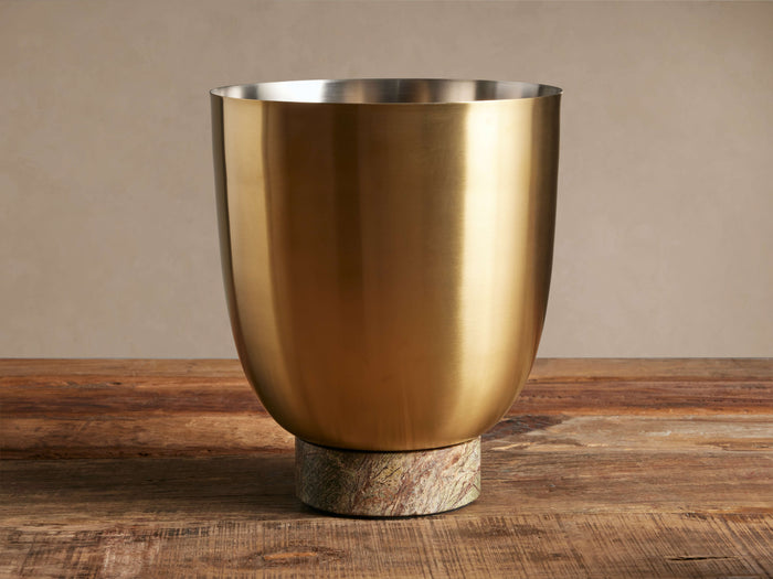 Gold stainless steel Rhodes Ice Bucket with a veined green marble base, sitting on a rustic wooden table.