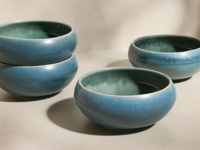 Four blue-green Rhoswen Cereal Bowls with reactive glaze finish. Two stacked on the left, two separate on the right.