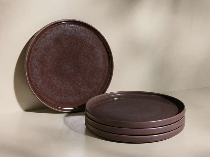 Front view of one deep plum reactive glaze Rhoswen Dinner Plate leaning upright, and three stacked deep plum Rhoswen Dinner Plates.