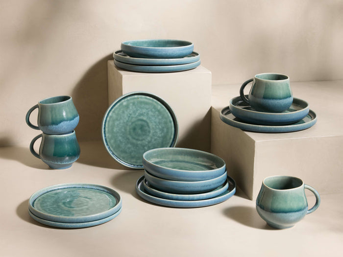 Full set of blue-green reactive glaze Rhoswen Dinnerware With Pasta Bowls, stacked and arranged on different levels.