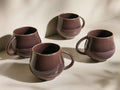 Angled view of four deep brown reactive glaze Rhoswen Mugs with unique tonal variations and organic shapes.