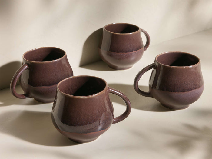 Angled view of four deep brown reactive glaze Rhoswen Mugs with unique tonal variations and organic shapes.