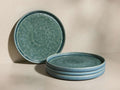 Teal-green Rhoswen Salad Plates, one standing upright, three stacked, showing reactive glaze and tonal variations.