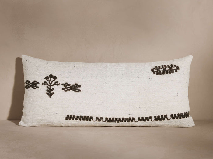 Rectangular white cushion with black geometric embroidery designs, including floral and linear patterns, against a neutral background.
