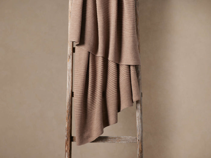 Warm taupe Rib Knit Throw with visible ribbed detailing, draped casually over a rustic wooden ladder against a light brown wall.