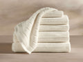 A stack of five neatly folded white towels, with a sixth towel draped over the top, displayed on a flat surface against a neutral background.