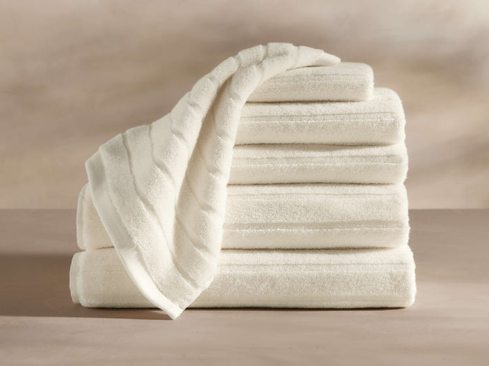 A stack of five neatly folded white towels, with a sixth towel draped over the top, displayed on a flat surface against a neutral background.