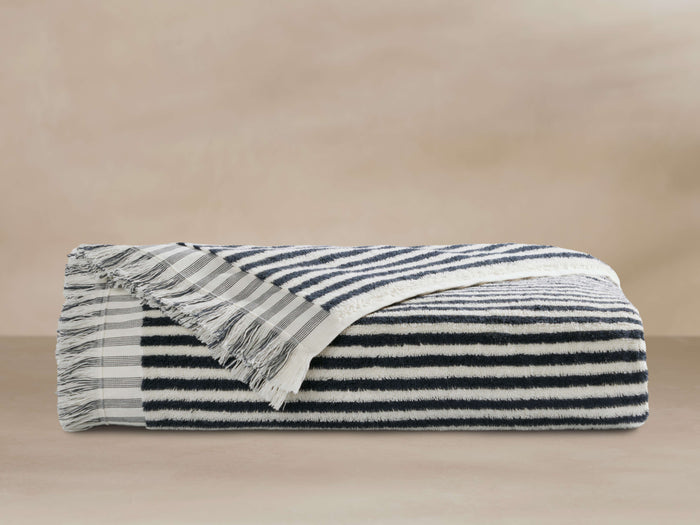 Rivi Beach Towel folded, showing indigo and white stripes, with fringed edges, lying on a plain surface.