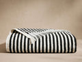 Rivi Beach Towel, folded showing classic black and white vertical stripes and fringe edge detail, on a neutral background.