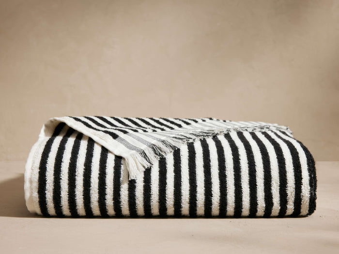 Rivi Beach Towel, folded showing classic black and white vertical stripes and fringe edge detail, on a neutral background.