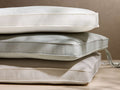 Stack of 3 Roos outdoor replacement cushions: off-white, light gray, and beige, with textured fabric, piped edges, and a tie strap.