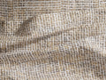 Roula Flat Sheet, close-up of folded fabric with abstract white, brown & gold mottled pattern. Visible stitched hem.