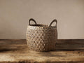 Round Entry Basket in Natural, handwoven seagrass, textured, with two top handles, on a rustic wooden table.