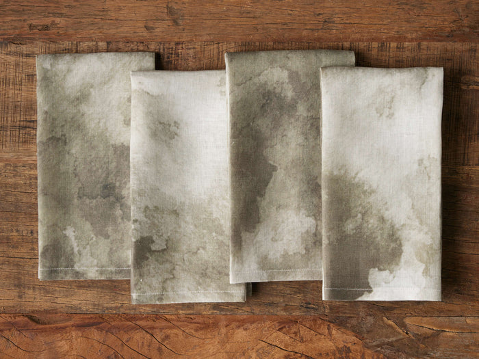 Sabine Napkins set with an abstract, watercolor-like pattern in muted grays and whites, folded neatly on a wooden surface.
