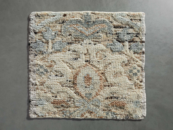Sadie Hand-Knotted Rug Swatch on a gray surface, showcasing soft blue, beige, and cream colors with an abstract pattern.
