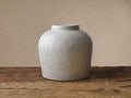 White Santorini Low Vase, round, crackle-glazed terracotta, on a rustic wooden surface against a neutral beige wall.