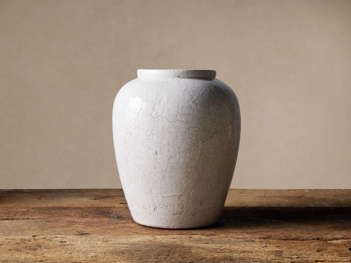 White Santorini Urn with crackle glaze, standing upright on a distressed wooden table against a light tan wall.