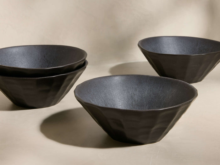 Front view of four black Saskia Cereal Bowls. Two bowls are stacked, two separate, featuring faceted sides and textured interiors.