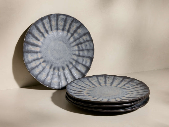 One Saskia Dinner Plate stands upright, three stacked. Dark blue-grey with a light radiating textural pattern and organic edges.