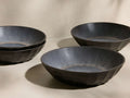 Four dark grey Saskia Pasta Bowls, two stacked, two separate, featuring faceted exteriors and speckled blue-grey interiors.
