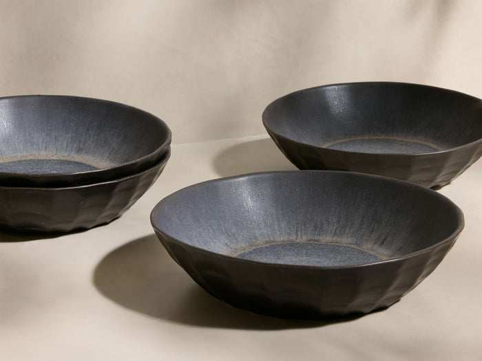 Four dark grey Saskia Pasta Bowls, two stacked, two separate, featuring faceted exteriors and speckled blue-grey interiors.