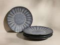 Set of four blue-grey Saskia Salad Plates. One stands upright, three are stacked, featuring a radial pattern and speckled finish.