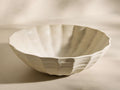 Front view of the off-white, fluted Saskia Serving Bowl with a wavy rim and textured surface.