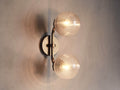 Sayre Double Sconce in plated Burnished Brass with two ribbed glass globes, mounted horizontally, emitting warm light.